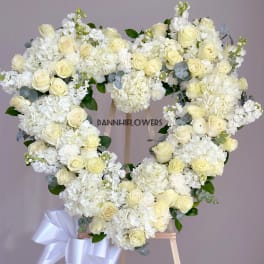 Heart-shaped white floral wreath on an easel with a ribbon bow