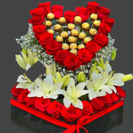 Heart-shaped rose and chocolate arrangement with white lilies in a black box