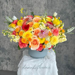 Large mixed bouquet in a ribbed blue vase with yellow, peach, pink, and white blooms