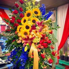Large standing floral spray with sunflowers, red roses, and blue flowers