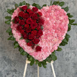 Heart-shaped floral tribute with red roses and pink carnations on an easel