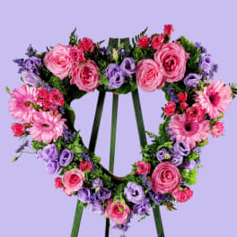 Heart-shaped floral wreath on a green easel with pink and purple flowers