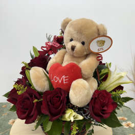 Teddy bear with a red heart surrounded by red roses in a basket