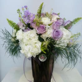 Lavender roses and white hydrangeas in a tall vase with fern accents