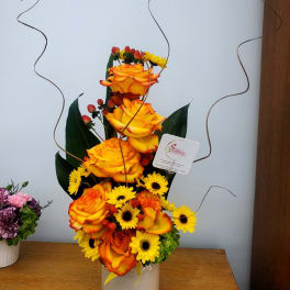 Tall arrangement of orange roses and yellow daisies in a white vase