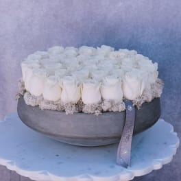 Round arrangement of white roses in a gray bowl with a ribbon