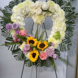 Heart-shaped floral wreath on an easel with white, pink, purple, and yellow flowers