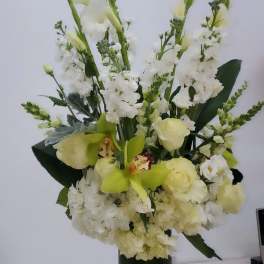 Tall white floral arrangement in a dark green vase with pale green orchids and roses