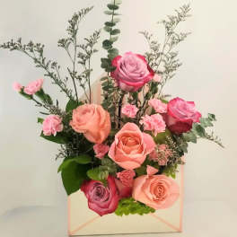 Pink and peach roses arranged in a pastel gift box with greenery