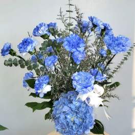 Blue carnations and hydrangea in a glass vase with a white ribbon