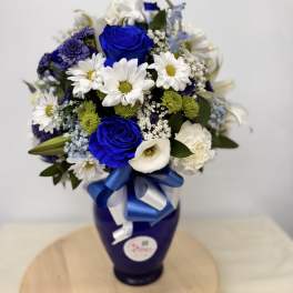 Blue and white flower bouquet in a dark vase with a ribbon