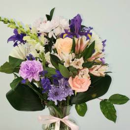 Mixed bouquet of pastel flowers in a clear glass vase with a pink ribbon