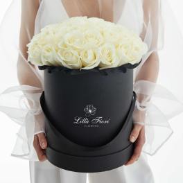 White roses arranged in a black round box with sheer ribbon