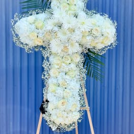 White floral cross arrangement on an easel with palm fronds