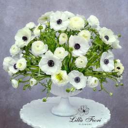 White anemones and ranunculus arranged in a white pedestal vase