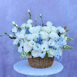 White floral arrangement in a woven basket with a ribbon bow