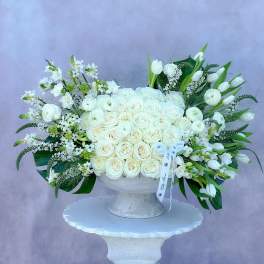 Large white rose arrangement in a white pedestal vase