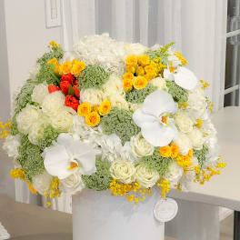 Large white floral arrangement with yellow and red roses in a white hatbox