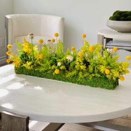 Low rectangular floral arrangement with yellow blooms on a table