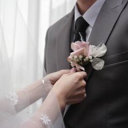 Bride pinning a pink boutonniere on a groom's suit