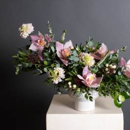 Pink orchid arrangement in a white pedestal vase