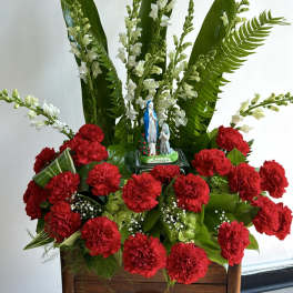 Red carnations with white flowers and a small Lourdes statue in a wooden container