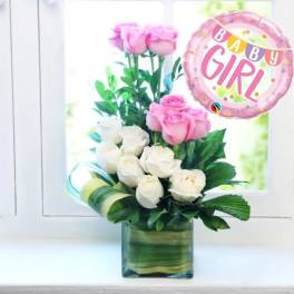 Pink and white roses in a square glass vase with a pink 'Baby Girl' balloon.