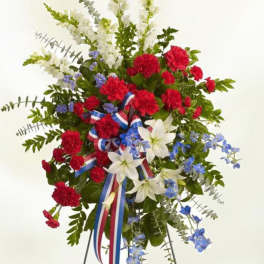 Tall red, white, and blue standing spray of flowers on a metal easel with a patriotic ribbon.