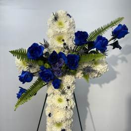 Cross-shaped floral tribute with white chrysanthemums and blue roses on an easel