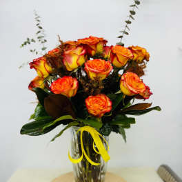 Bouquet of orange and yellow roses in a clear glass vase with a yellow ribbon