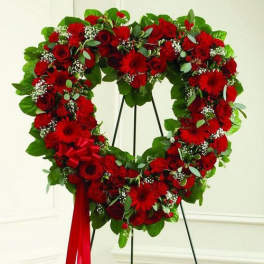 Heart-shaped standing wreath of red roses and other red flowers with a red ribbon bow.