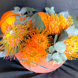 Orange flowers arranged in a football-shaped container with eucalyptus
