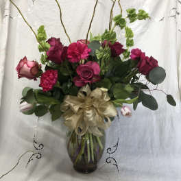 Pink and burgundy roses with carnations in a glass vase with a gold bow