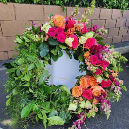 Large green wreath with bright pink and orange roses and accent flowers on one side