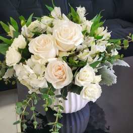 White and cream rose arrangement with greenery in a white textured pot on a black table