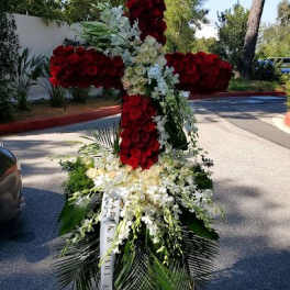 Tall standing cross of red and white flowers on an easel with cascading white blooms
