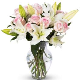 Vase arrangement of pale pink roses and white lilies in a clear glass vase with visible stems