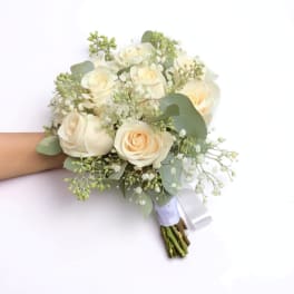 Handheld bouquet of cream roses with small white filler flowers wrapped in white ribbon.