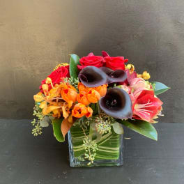 Mixed bouquet with red roses, black calla lilies, and orange tulips in a glass vase