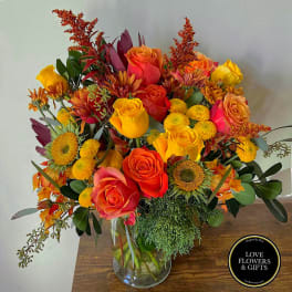 Vibrant arrangement of orange and yellow roses with yellow mums in a clear glass vase