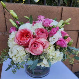 Round arrangement of pink roses, white hydrangeas, and lisianthus in a clear glass vase