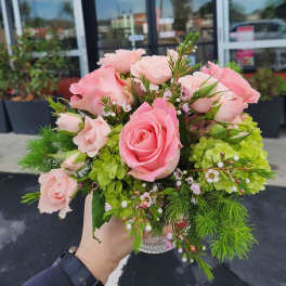 Small bouquet of pink roses with green hydrangea in a clear glass vase held outdoors.