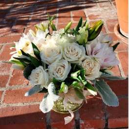 Low glass vase of white roses and pale blooms arranged in a rounded cluster