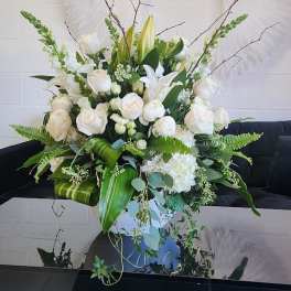 Large white and green floral arrangement with roses, lilies, and snapdragons in a white vase