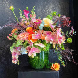Mixed bouquet of pink orchids, roses, and calla lilies in a green vase