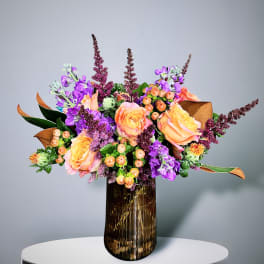 Bouquet of peach roses and purple flowers in a ribbed glass vase