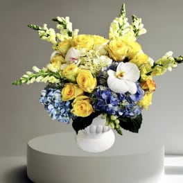 Yellow roses and blue hydrangeas in a white vase