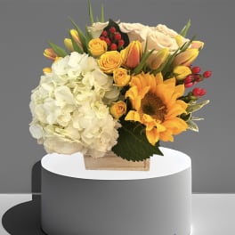 Bouquet of white hydrangeas, yellow roses, and a sunflower in a wooden box