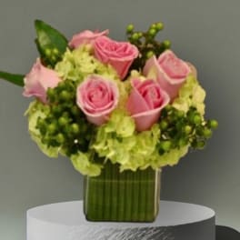 Pink roses arranged with pale green hydrangeas in a clear square vase