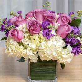 Pink roses and white hydrangeas in a square glass vase with purple accents